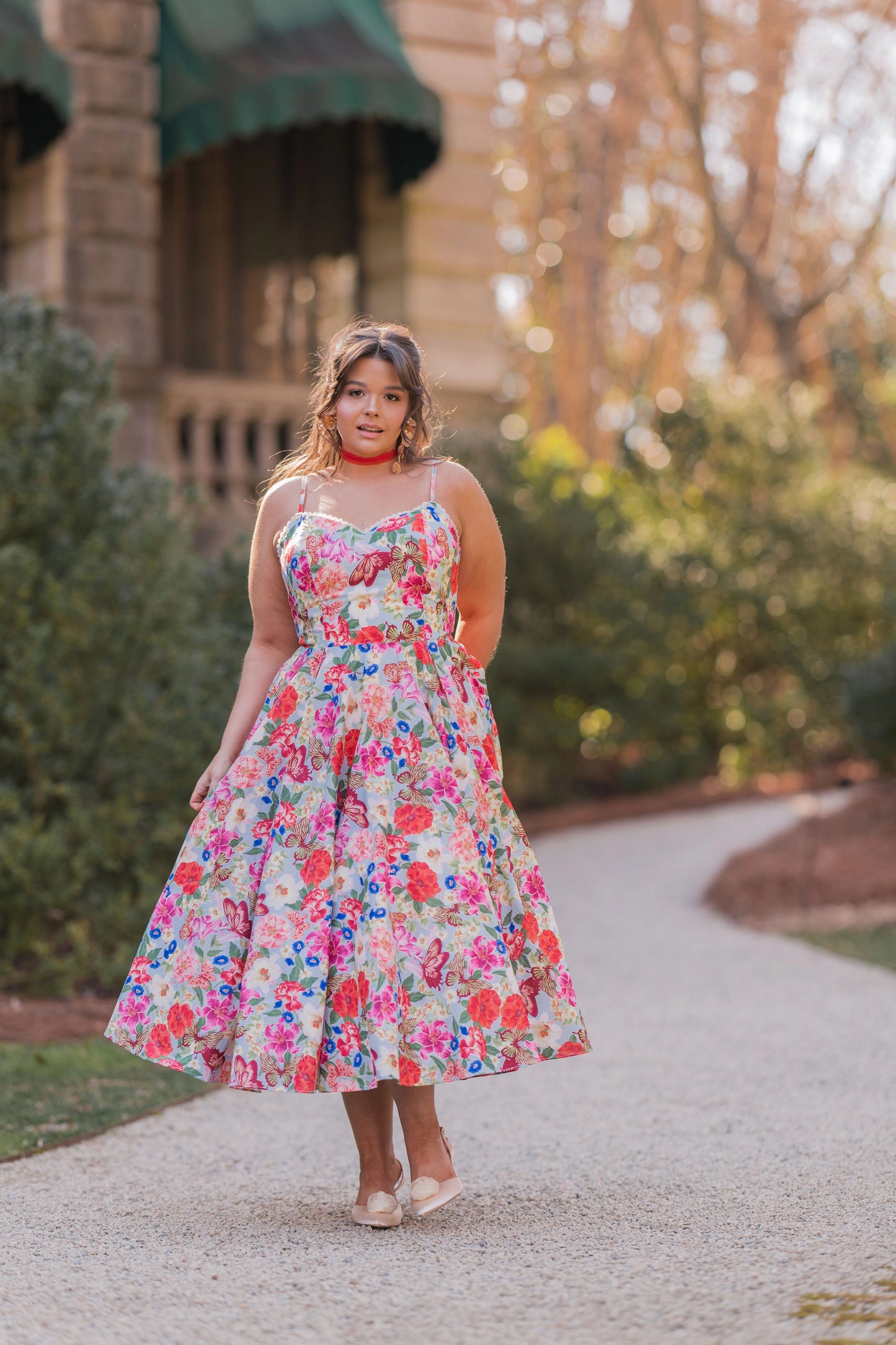 The image shows a woman in a colorful dress walking down a path surrounded by trees and a building in the background. She is wearing a pair of footwear, suggesting she is ready to take on the world.