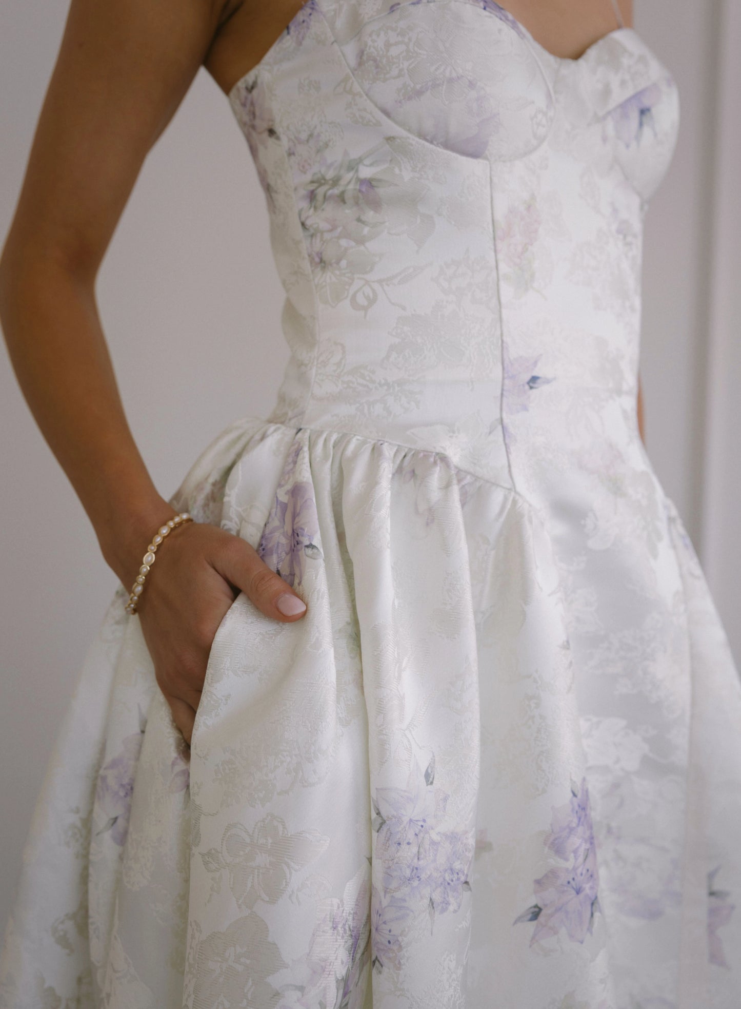 Woman wearing white floral dress with sweetheart neckline and spaghetti straps, posing with hand in pocket.