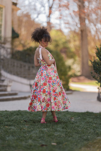The image shows a woman in a colorful dress walking down a path surrounded by trees and a building in the background. The woman is wearing a dress with a variety of colors, including blues, greens