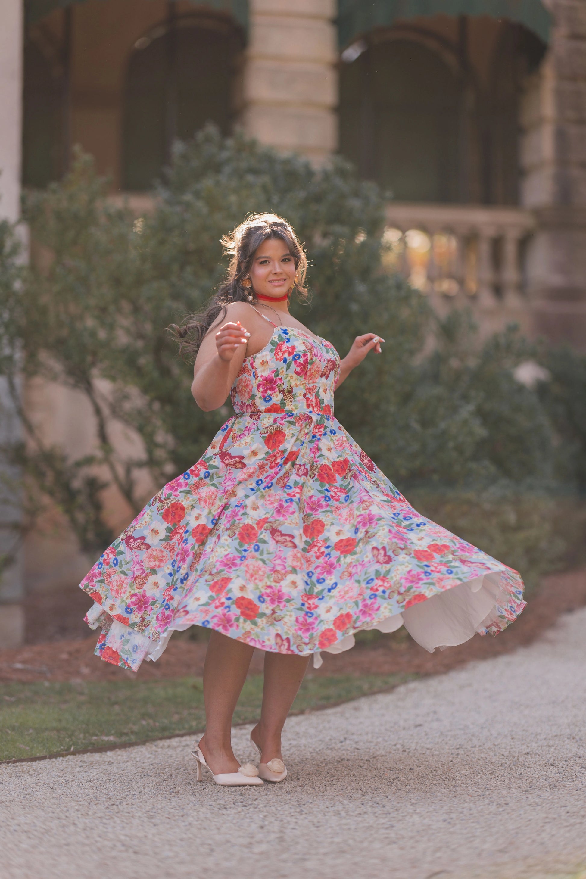 The image shows a woman in a colorful dress walking down a street, with a building and trees in the background. She is wearing footwear, suggesting she is ready to take on the world.
