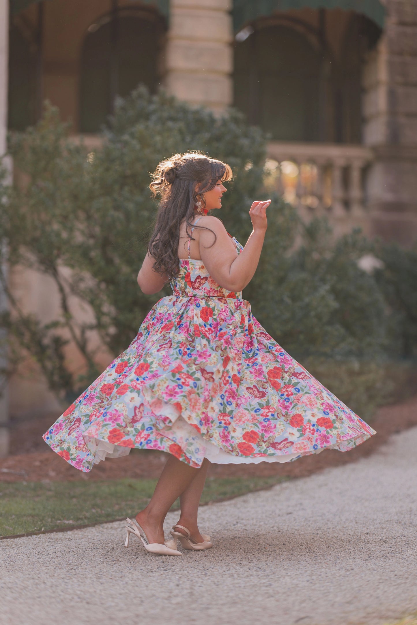 The image shows a woman in a colorful dress walking down a sidewalk, surrounded by trees and a building in the background. She is wearing a dress with a unique design, likely inspired by the popular