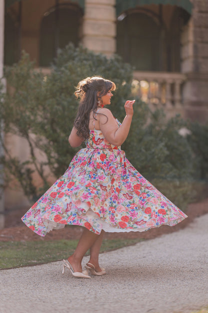The image shows a woman in a colorful dress walking down a sidewalk, surrounded by trees and a building in the background. She is wearing a dress with a unique design, likely inspired by the popular
