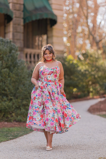 The image shows a woman in a colorful dress walking down a path in front of a building, surrounded by trees and a clear blue sky. The image is slightly blurred, giving it a dreamy, ethereal feel.